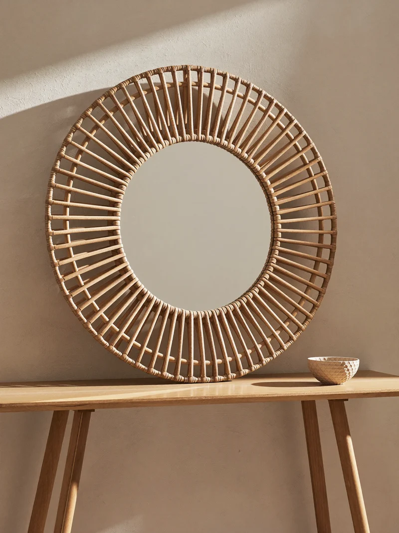 Specchio tondo con cornice in rattan appoggiato a una parete intonacata