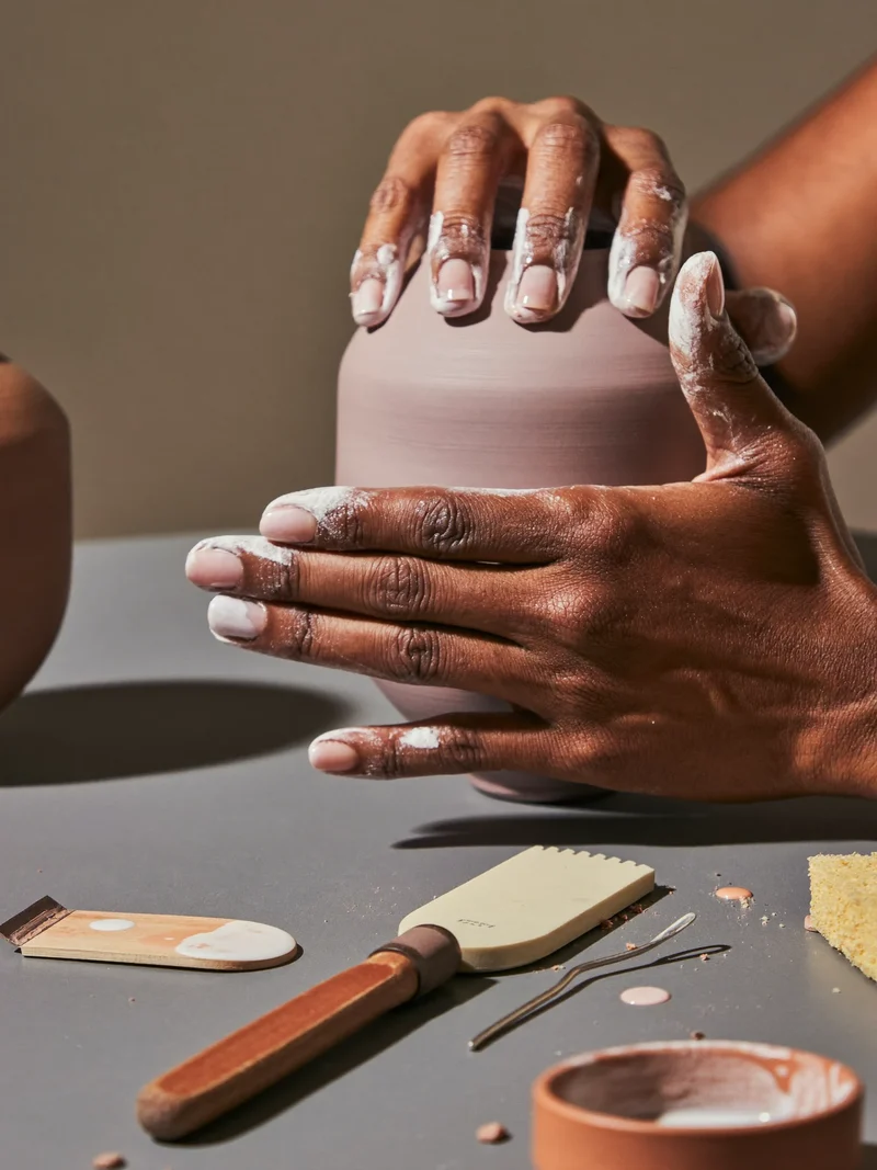 Mani di artigiano che smaltano un vaso in ceramica sul banco